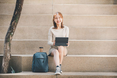 Portrait of young woman using digital tablet sitting on steps outdoors