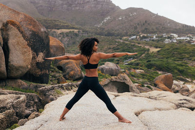 Rear view of woman exercising on rock