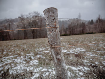 Wooden post on snow covered field against sky
