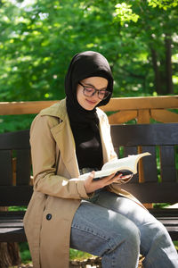 Young woman using phone while sitting on bench