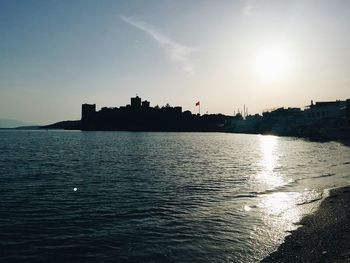 Silhouette city by sea against clear sky during sunset