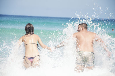 Rear view of friends splashing water at sea shore