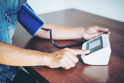 Midsection of woman using blood pressure machine at table