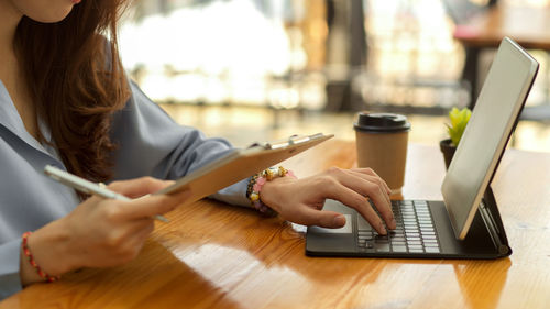 Midsection of woman using laptop at cafe