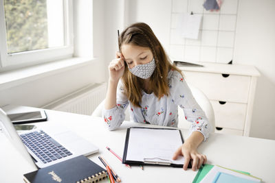 Young woman using phone while sitting on table at home