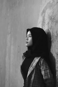 Side view of a young woman looking away against wall