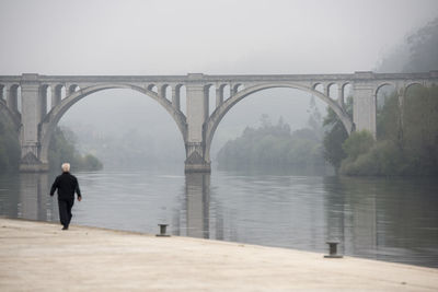 Man standing on bridge over river against sky