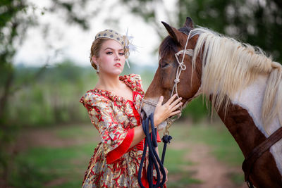 Woman in traditional clothing standing by horse against tree