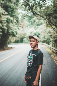 Portrait of young man standing on road against trees