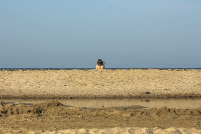 Rear view of woman at beach against clear sky