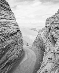 Distant view of woman standing on mountain peak against cloudy sky