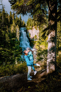 Side view of couple kissing while standing by trees in forest