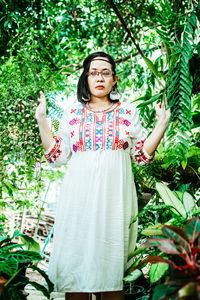 Portrait of young woman standing against plants