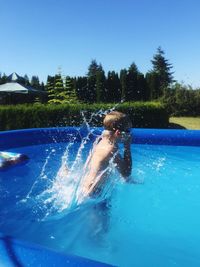 Side view of boy jumping in swimming pool against clear blue sky