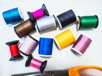 Directly above shot of multi colored spool with scissors over white background