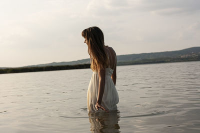 Woman standing in sea against cloudy sky