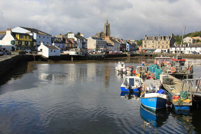 Boats moored in sea by buildings against sky