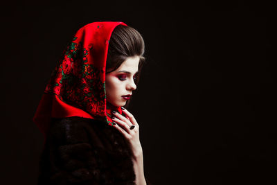 Side view of woman wearing red scarf against black background