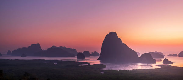 Rock formation in sea against sky during sunset