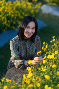 Portrait of smiling young woman with yellow flower in field