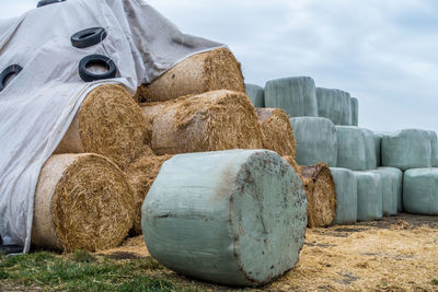 Stack of hay bales on field against sky