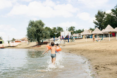 Rear view of boys running at beach against sky