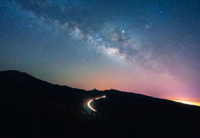 Amazing scenery of illuminated road with traffic lights in dark highlands under spectacular sky with stars in tenerife