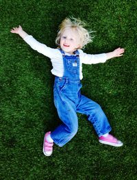 High angle portrait of smiling cute girl relaxing on grassy field