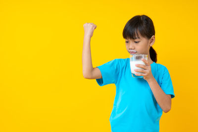 Full length of a boy drinking glass against yellow background