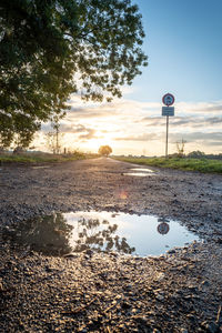 Road sign by lake against sky