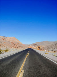 Road amidst desert against clear blue sky