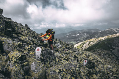 People on rock by mountains against sky