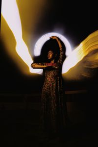 Midsection of woman standing against illuminated lights at night