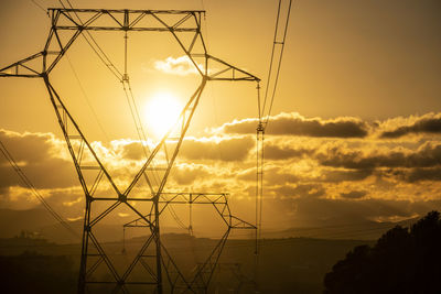 Low angle view of electricity pylon against sky during sunset