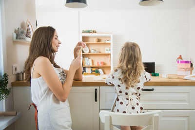 Mother photographing daughter preparing food on table at home