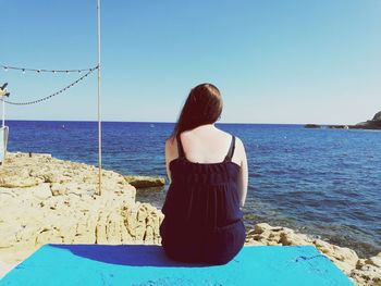 Rear view of woman on beach against clear blue sky