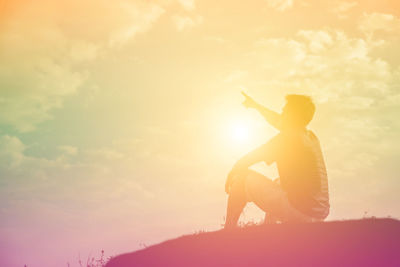 Side view of silhouette boy sitting against sky during sunset