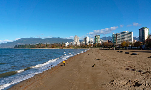 Scenic view of beach by buildings against blue sky