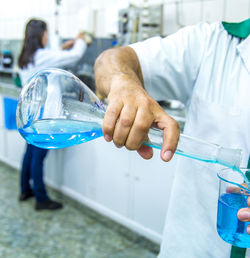 Midsection of scientist pouring liquid in beaker at laboratory