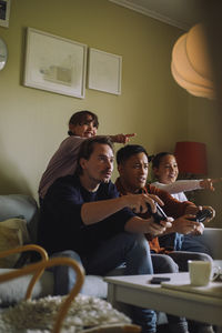 Serious gay men playing video game with daughters pointing at home