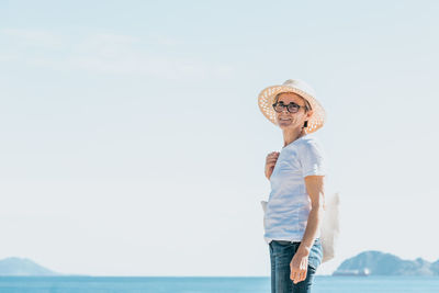 Side view of woman standing against sea against clear sky