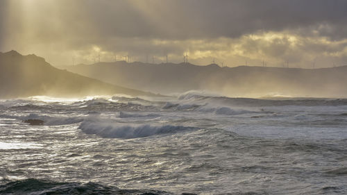 Big waves break on the coast, in the sunlit sea, passing through the clouds. galicia, spain.