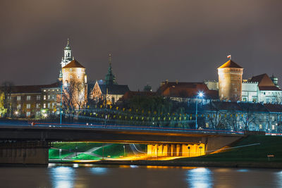 Illuminated buildings by river against sky in city at night