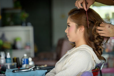 Cropped hands of hairdresser styling woman hair