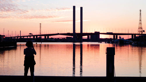 Silhouette man standing on bridge against sky during sunset