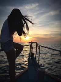 Woman sitting on railing in boat against sky during sunset