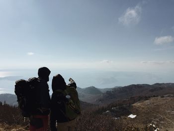 Rear view of hikers standing on mountain against sky