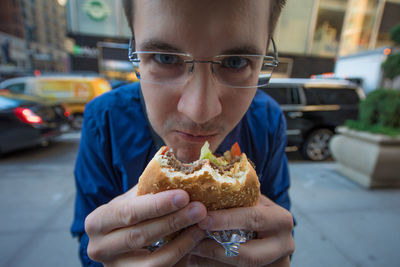 Portrait of man eating burger on roadside at city