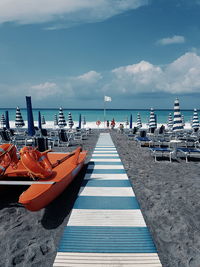 Diminishing perspective of footpath at beach against sky during sunny day