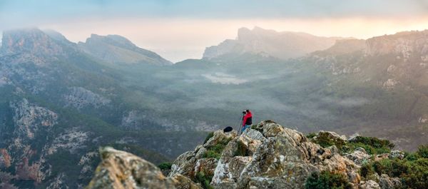 People on rocks by mountains against sky